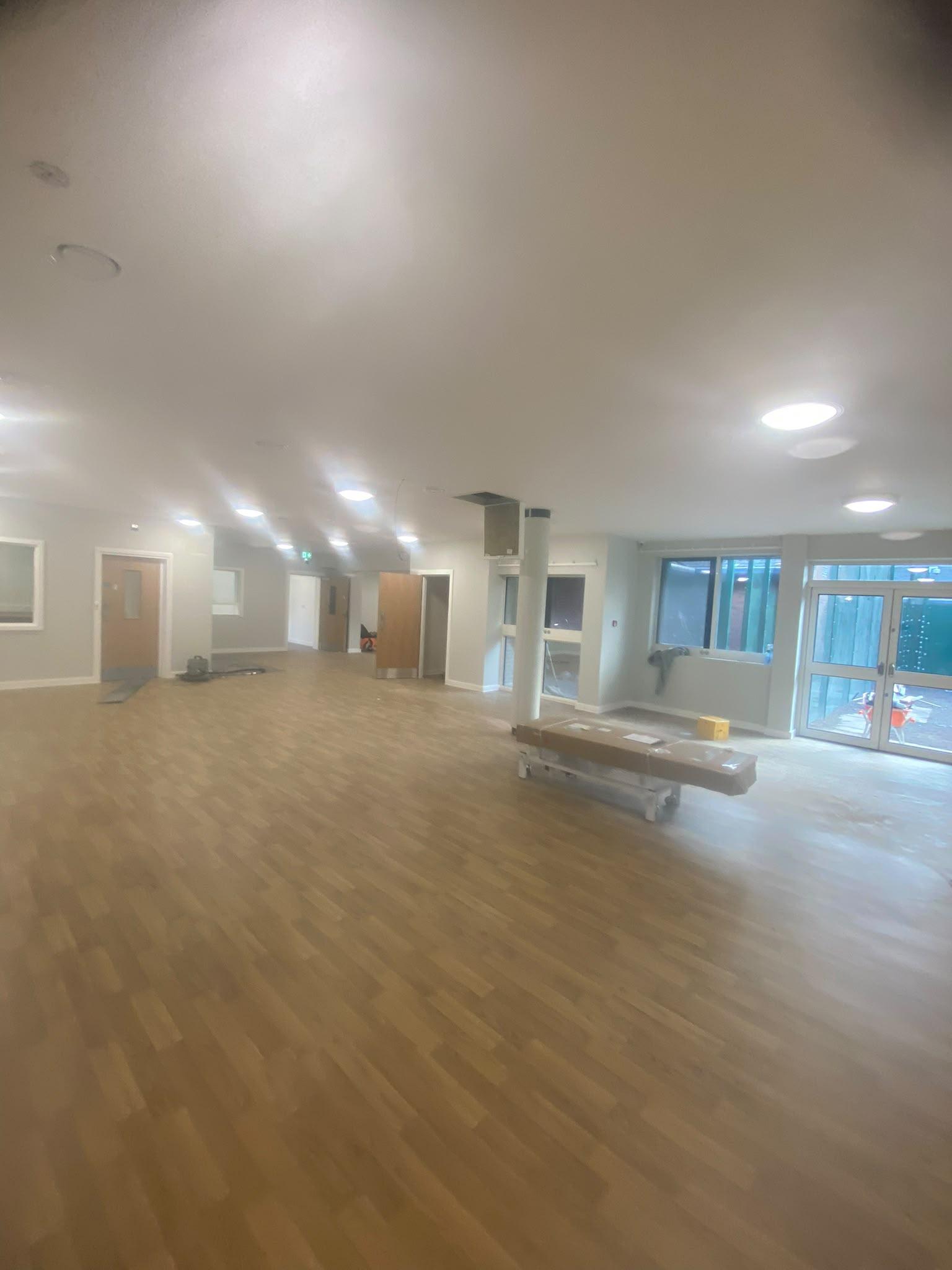 Open plan commercial hall painted soft grey green with a white ceiling and oak fire doors
