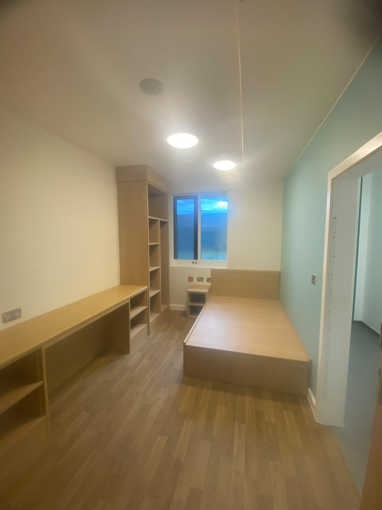 Study bedroom with fitted birch ply furniture, cream walls and a mint green feature wall