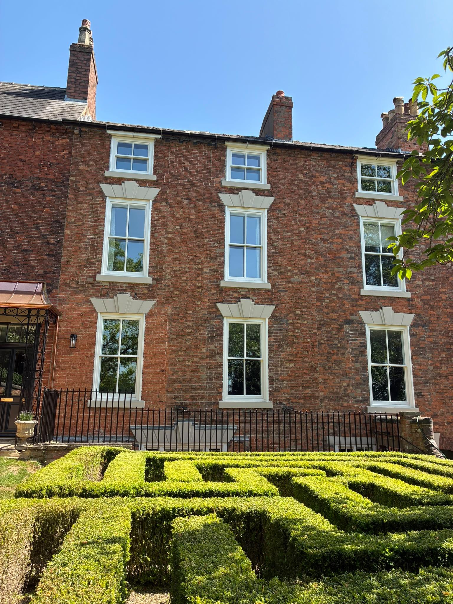 Edwardian red brick house with freshly painted soft white sash windows and stone lintels, box hedge garden in front