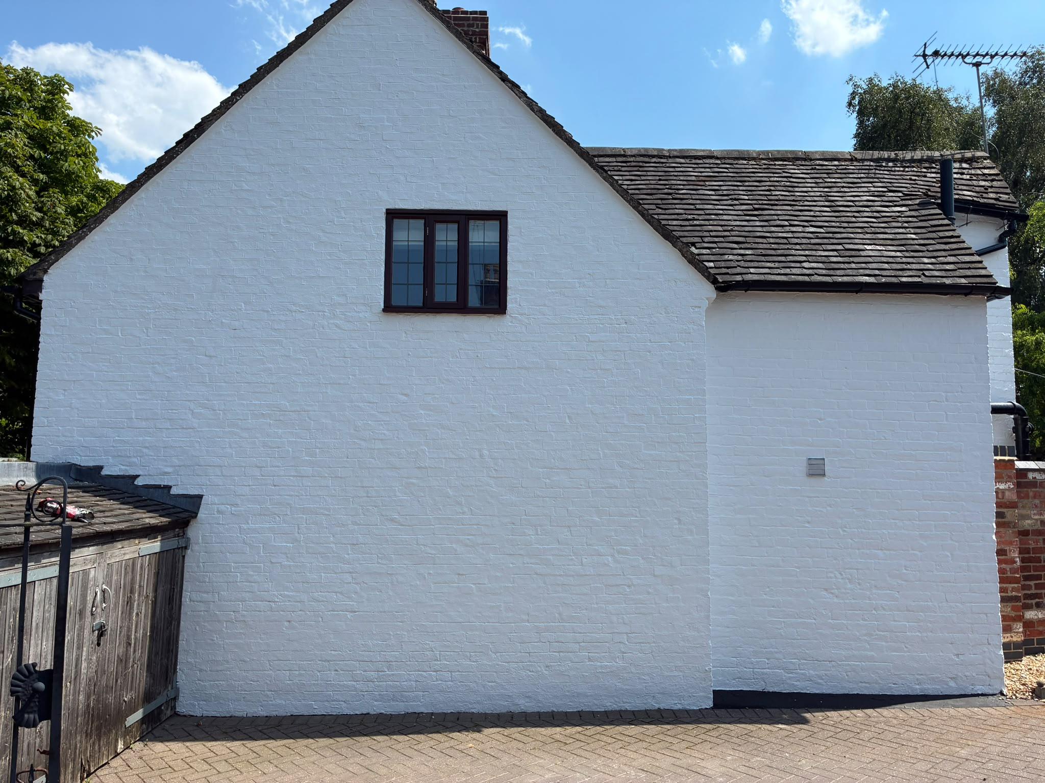Brick cottage gable painted brilliant white with a black plinth, clay tile roof and blue sky