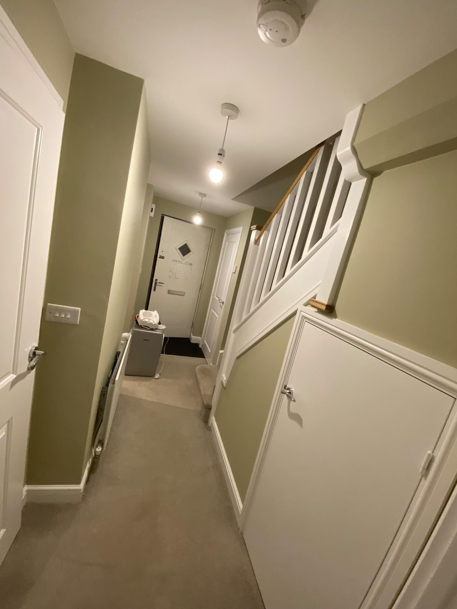 Hallway and staircase painted olive green with white spindles, panelling and an oak handrail