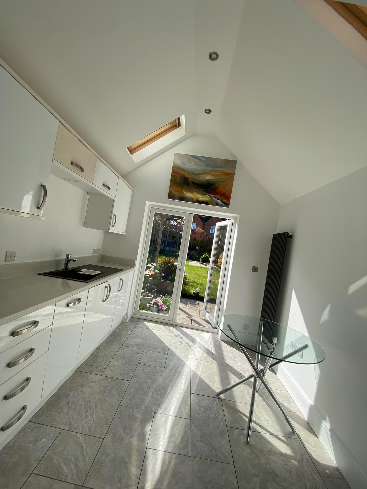 Bright white vaulted kitchen extension with rooflight, French doors to the garden and gloss white units