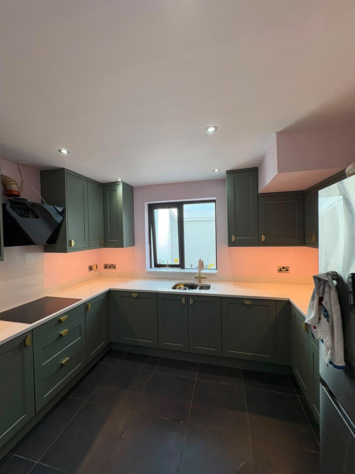 Dark green shaker kitchen with brass handles, blush pink walls and white quartz worktops