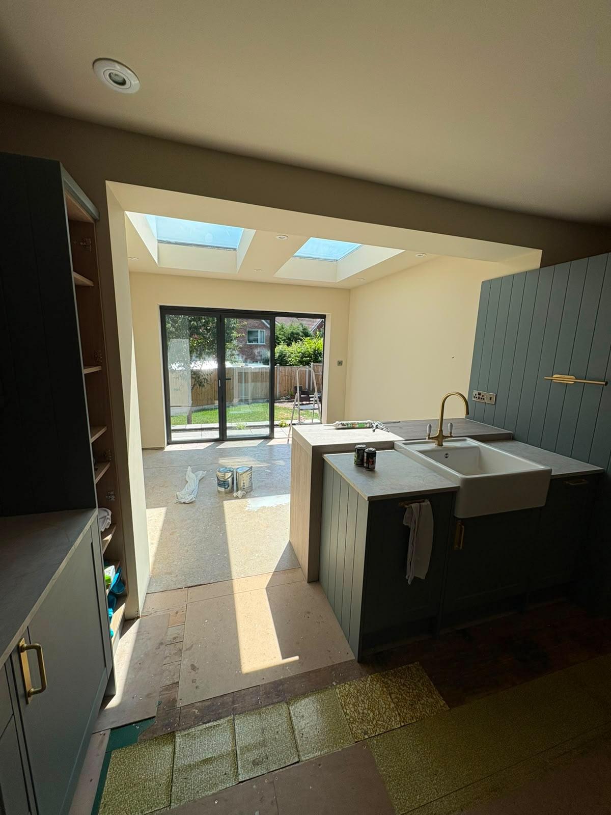 Blue grey shaker kitchen with a belfast sink opening into a rooflit extension with bifold doors