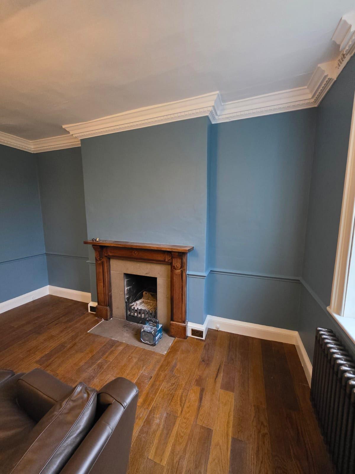 Victorian living room painted deep blue with ornate white cornice, timber fireplace and oak floor