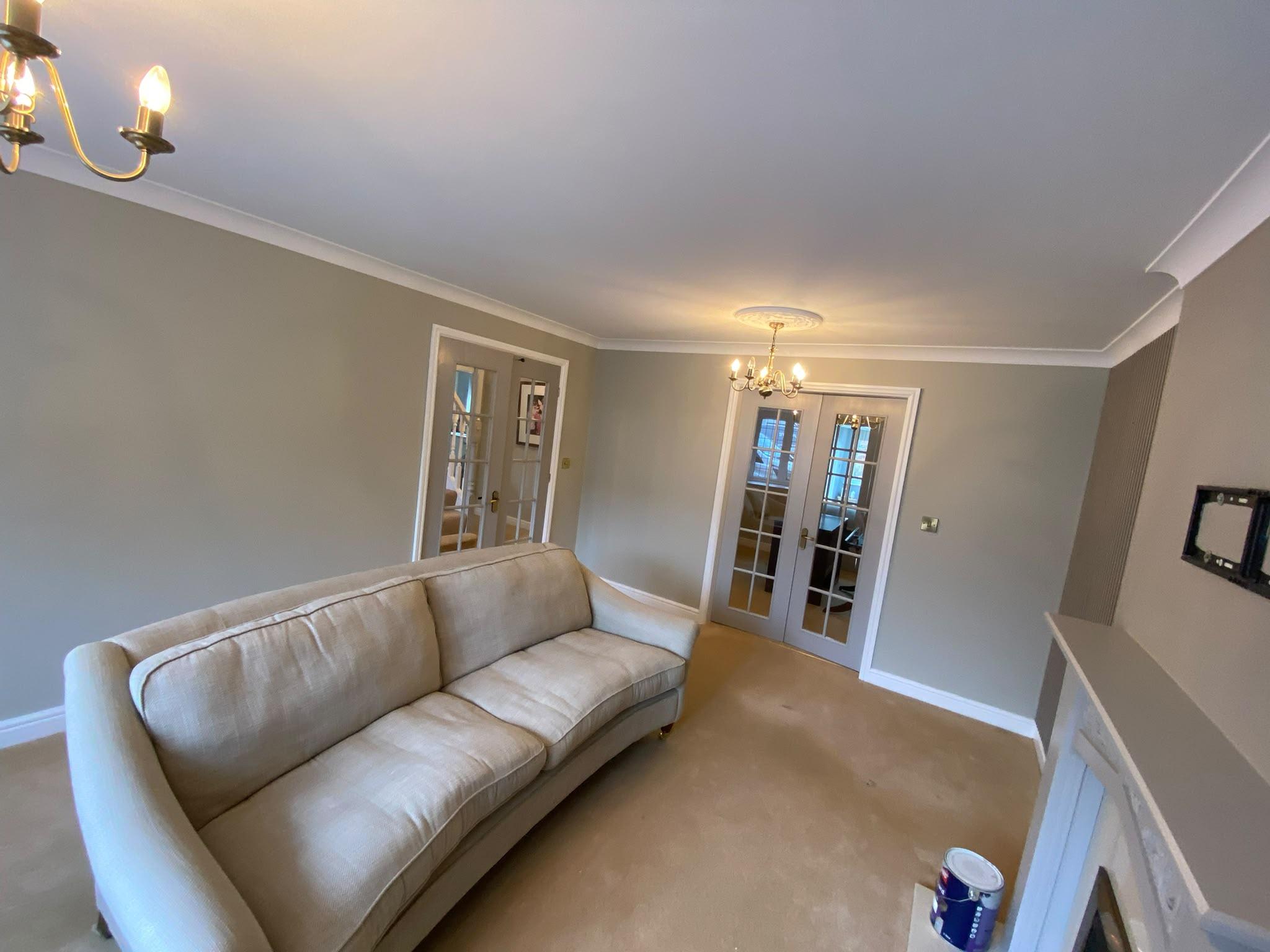 Large sitting room painted warm greige with white coving, ceiling rose and glazed French doors